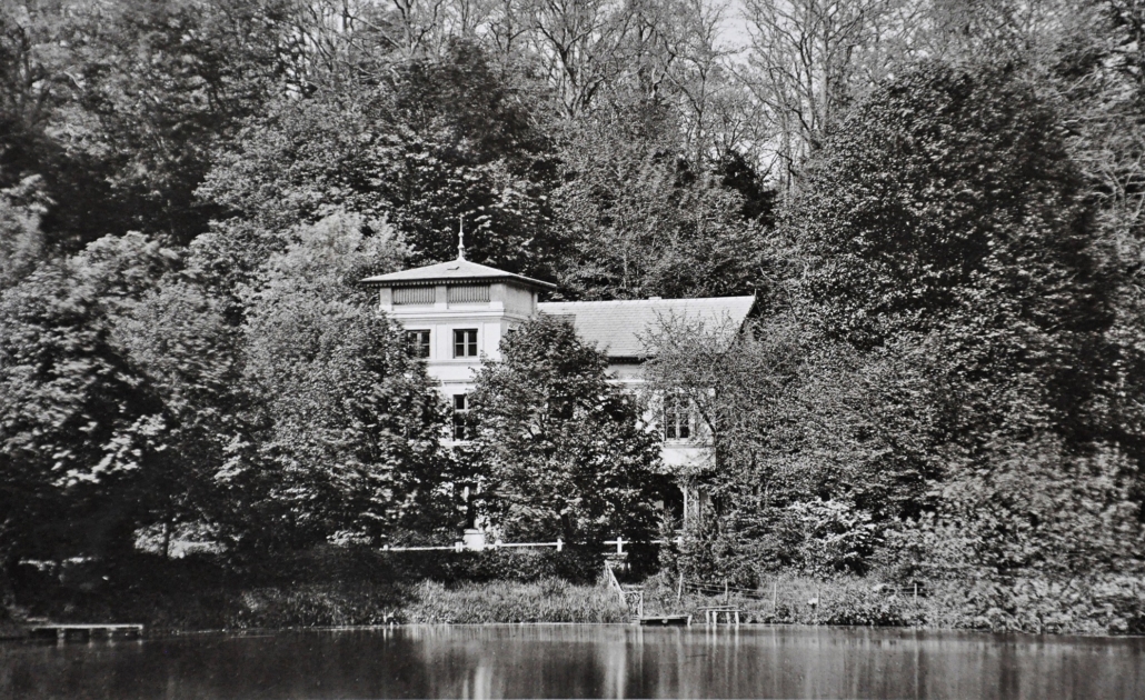 Auf der Schwarz-Weiß-Fotografie ist im Vordergrund der Friedrichsruher Schlossteich zu sehen und dahinter das sogenannte Turmhaus.