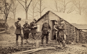 Secchs Soldaten stehen vor einer kleinen Hütten, die provisorisch aus Zweigen gebaut wurde.